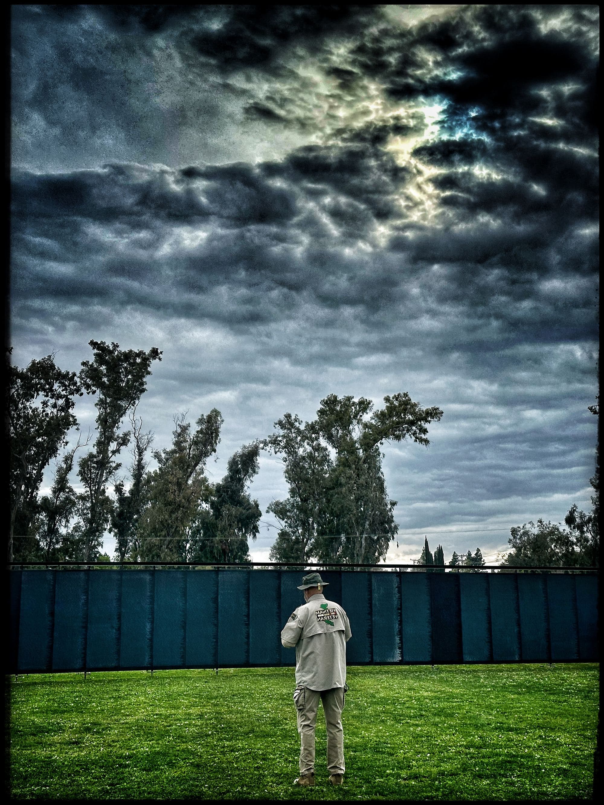 A Vietnam veteran stands before The Wall That Heals at dusk beneath a stormy sky